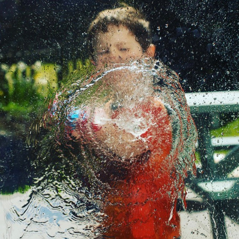 little boy spraying glass door with watergun in summer photo