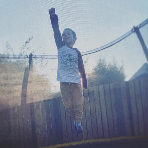 little boy in superman posed photographed on trampoline in summer