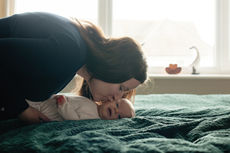 mother bending down to kiss baby daughter on bed