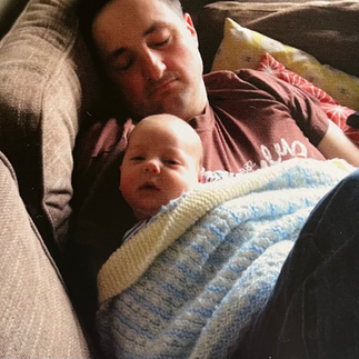 dad sleeping on sofa holding baby son in candid family photo