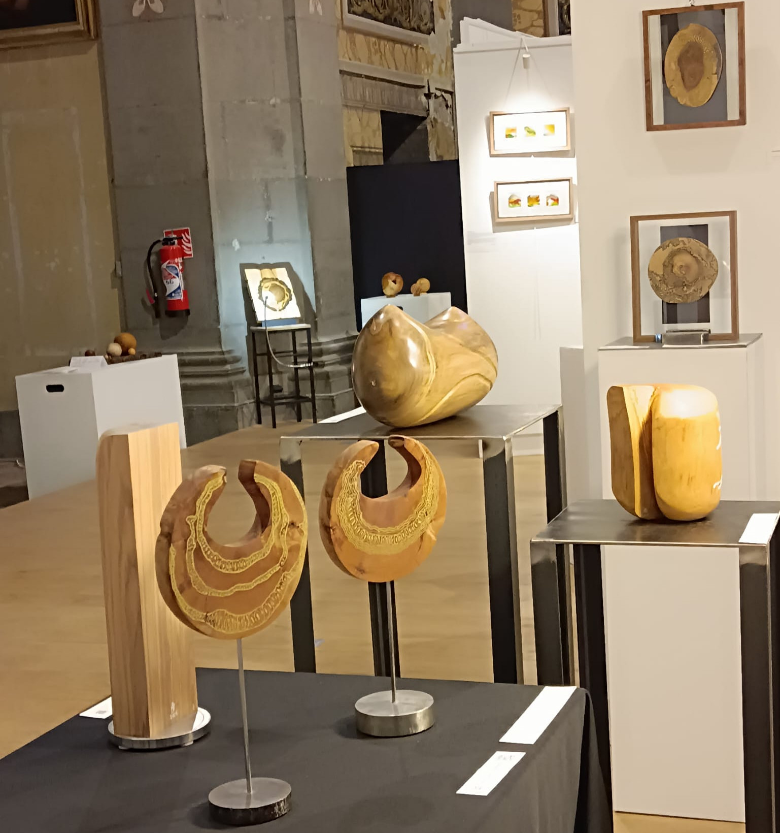 Ensemble de sculptures contemporaines en bois de Marie-Laure Teisseire présentées sur des socles et une table dans la Chapelle Vaugelas à Chambéry.