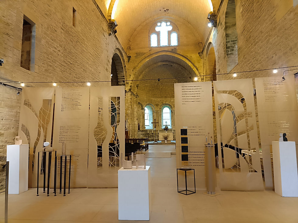 Vue intérieure de l’exposition « Vivre ! » dans l’église Saint-Pierre du prieuré de Marnans, avec des panneaux de scénographie, des sculptures et des œuvres présentées dans la nef.
