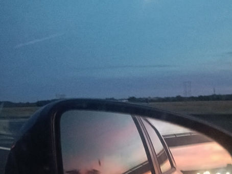 Route au crépuscule vue depuis une voiture, avec la lune dans le ciel et le reflet de la voiture dans le rétroviseur.