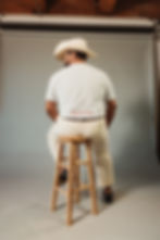 A man sitting on a stool while wearing a tshirt and a sombrero de vaquero.