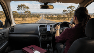 Woman driving a car on a long, country road with mobile phone mounted on the dashboard and lanyard placed on the passenger seat.