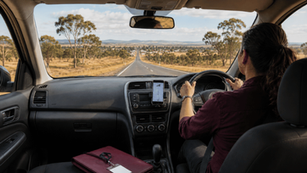 Woman driving a car on a long, country road with mobile phone mounted on the dashboard and lanyard placed on the passenger seat.