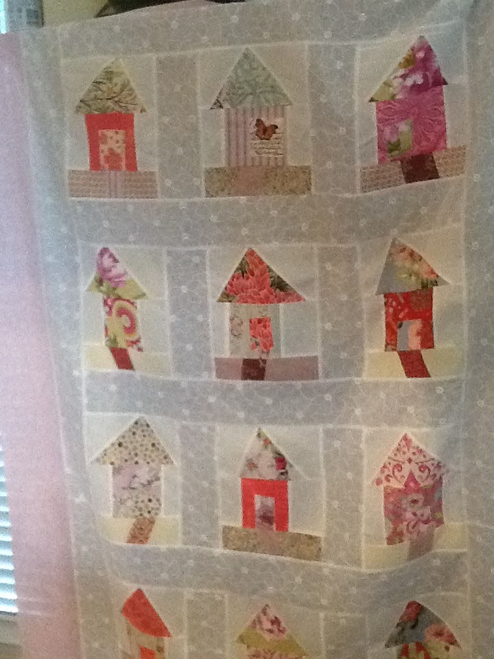 Modern improv style quilt with rows of colorful fabric house blocks on sheer white fabric, soft light, handmade and cozy.