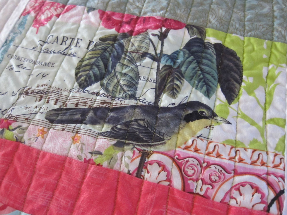 Colorful quilt close-up with a bird, leafy print, and French postcard-style text in pink, green, gray, and white patches