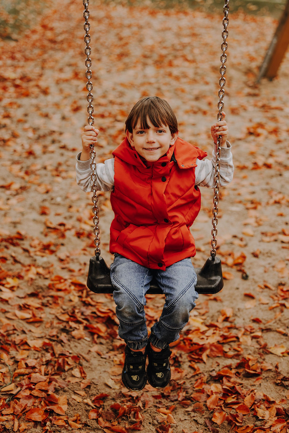 Junge auf Schaukel sitzt und lächelt, Herbstlaub parkt. KidoPic.de