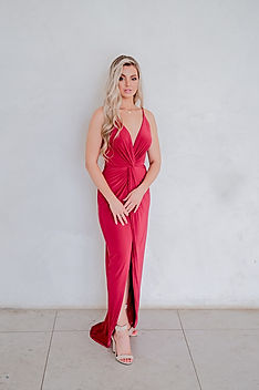 Bridesmaid wearing the Gelique Sam Knot Dress in bold ruby red — a sexy, modern bridesmaid gown featuring a plunging V-neckline, figure-flattering waist knot detail, and a tulip hemline that highlights the legs. This statement dress from Gelique Online is designed to turn heads with its sleek, feminine silhouette.