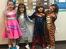 Four happy pre-k friends posing for a picture in their preschool classroom with costumes on.