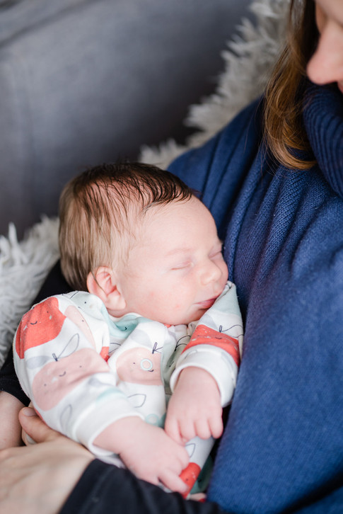 A baby in a bright babygrow sleeping in his mother's arms