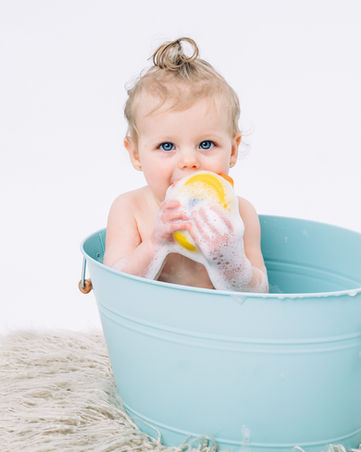baby girl chewing a rubber duck in a blue bathtub in white studio