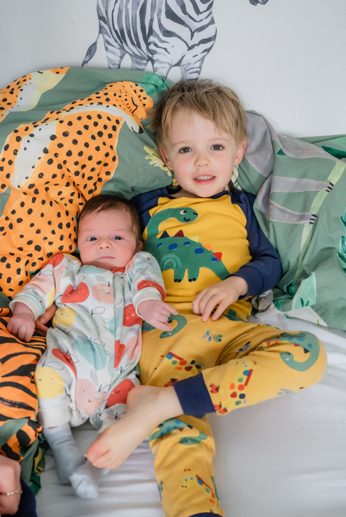 A young boy reclining in his bed with a newborn baby nestled beside him