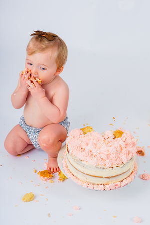 red haired girl in a a nappy cover eating cake with her hands