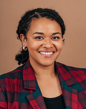 Smiling person in a red and green plaid jacket, hoop earrings, against a plain brown backg