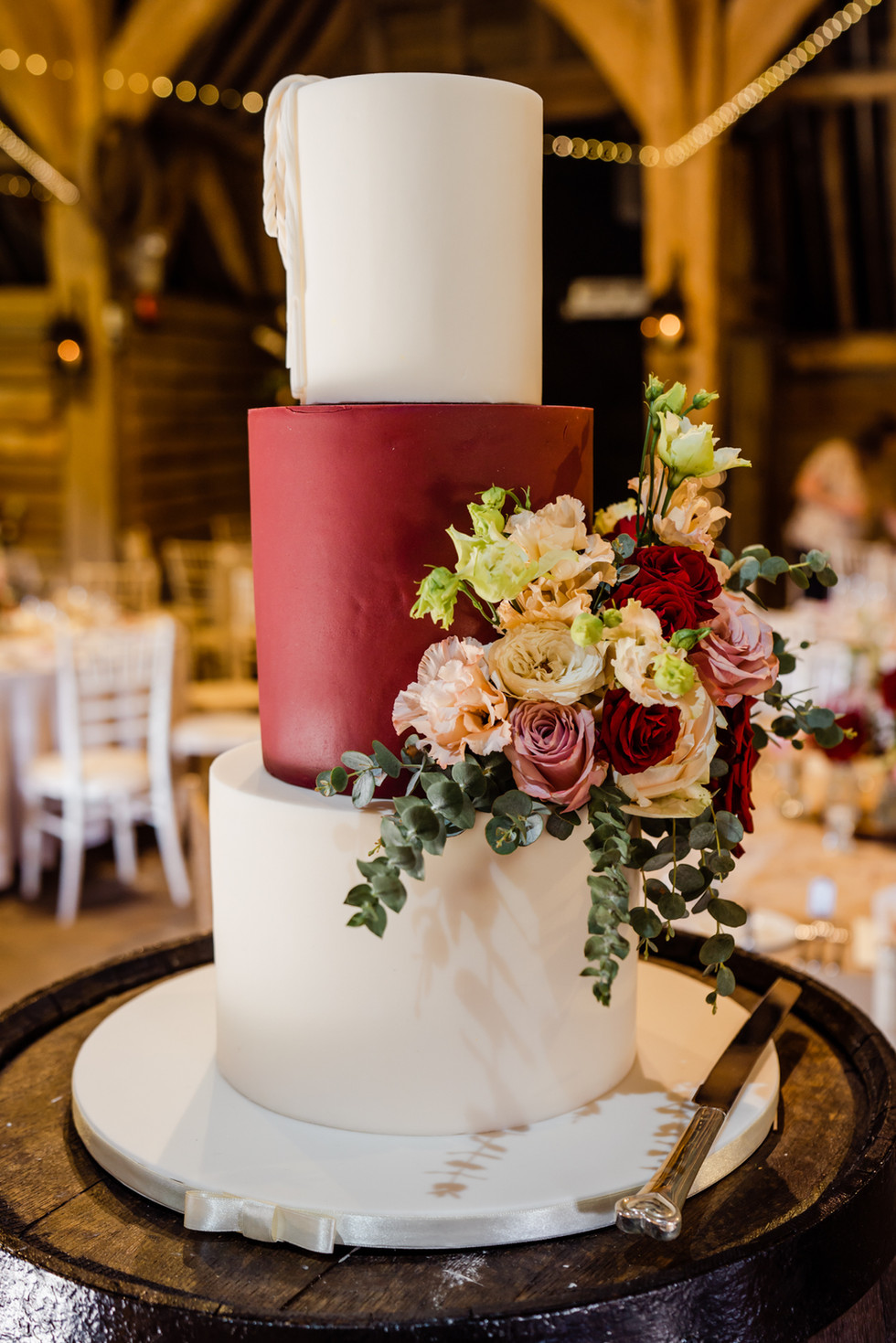 Three tier wedding cake decorated with red, white and pink flowers. Top and bottom cake have white icing and the middle tier has red icing