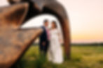 Wedding portrait of bride and groom framed by a bronze sculpture with sunset behind
