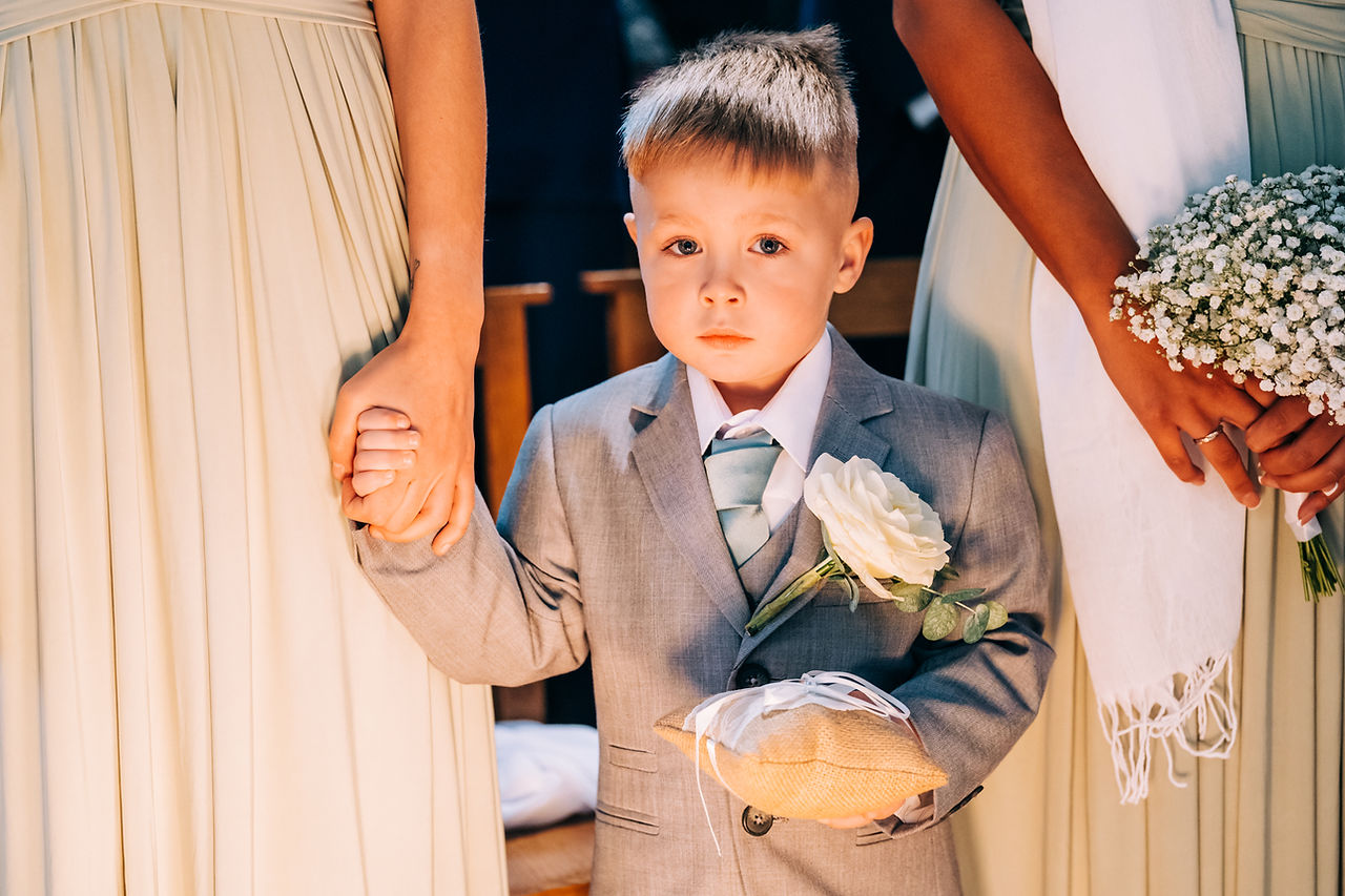 Young boy in grey suit holding cushion for wedding rings