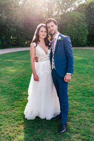 Bride and groom standing embracing on the grass with sunlight behind them