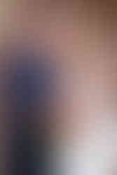 Close up portrait of a man in a navy suit and red tie embracing a bride in an off-the-shoulder white wedding dress and veil, carrying a bouquet of red, pink and cream flowers