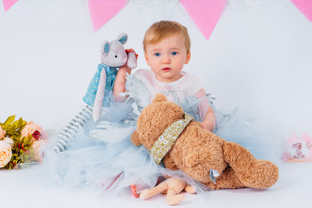 Red haired girl wearing a taffeta tutu surrounded by stuffed toys