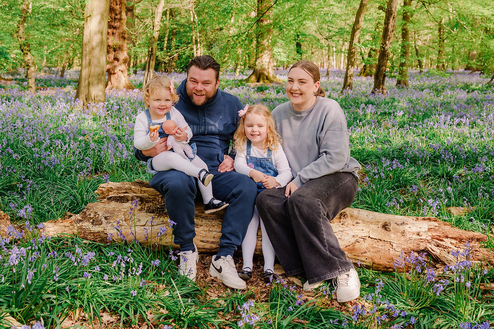 Family of four sitting on a log in a forest, surrounded by purple flowers. They are smiling, creating a warm, joyful atmosphere.