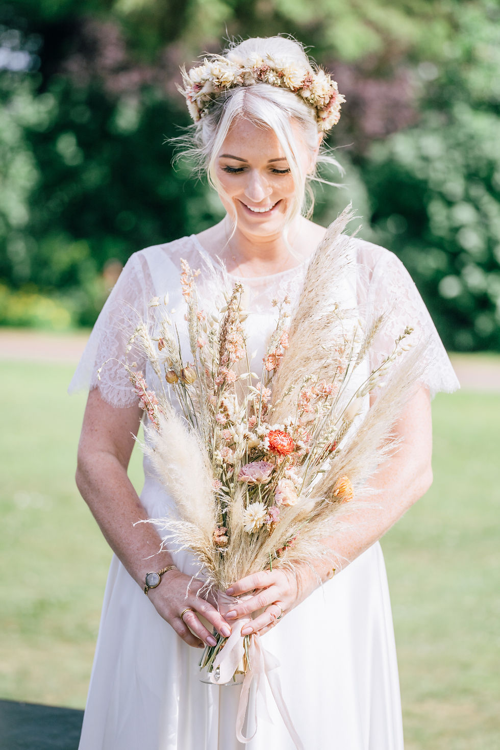 Blonde bride wearing a dried flower crown smiling down at her dried flower and grasses bouquet