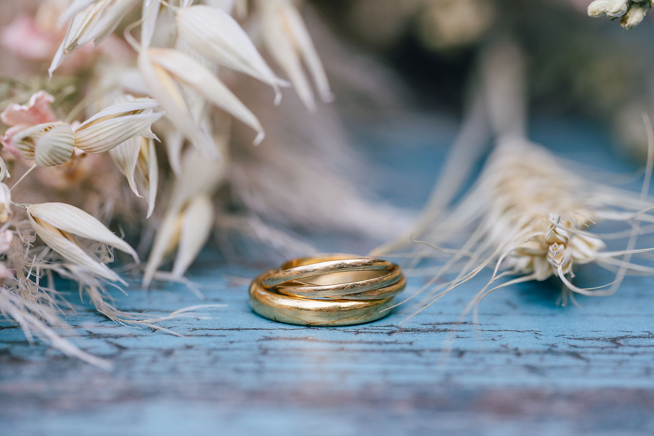 Extreme close up of 3 intertwined bands wedding ring on a turquoise table surrounded by dried grasses