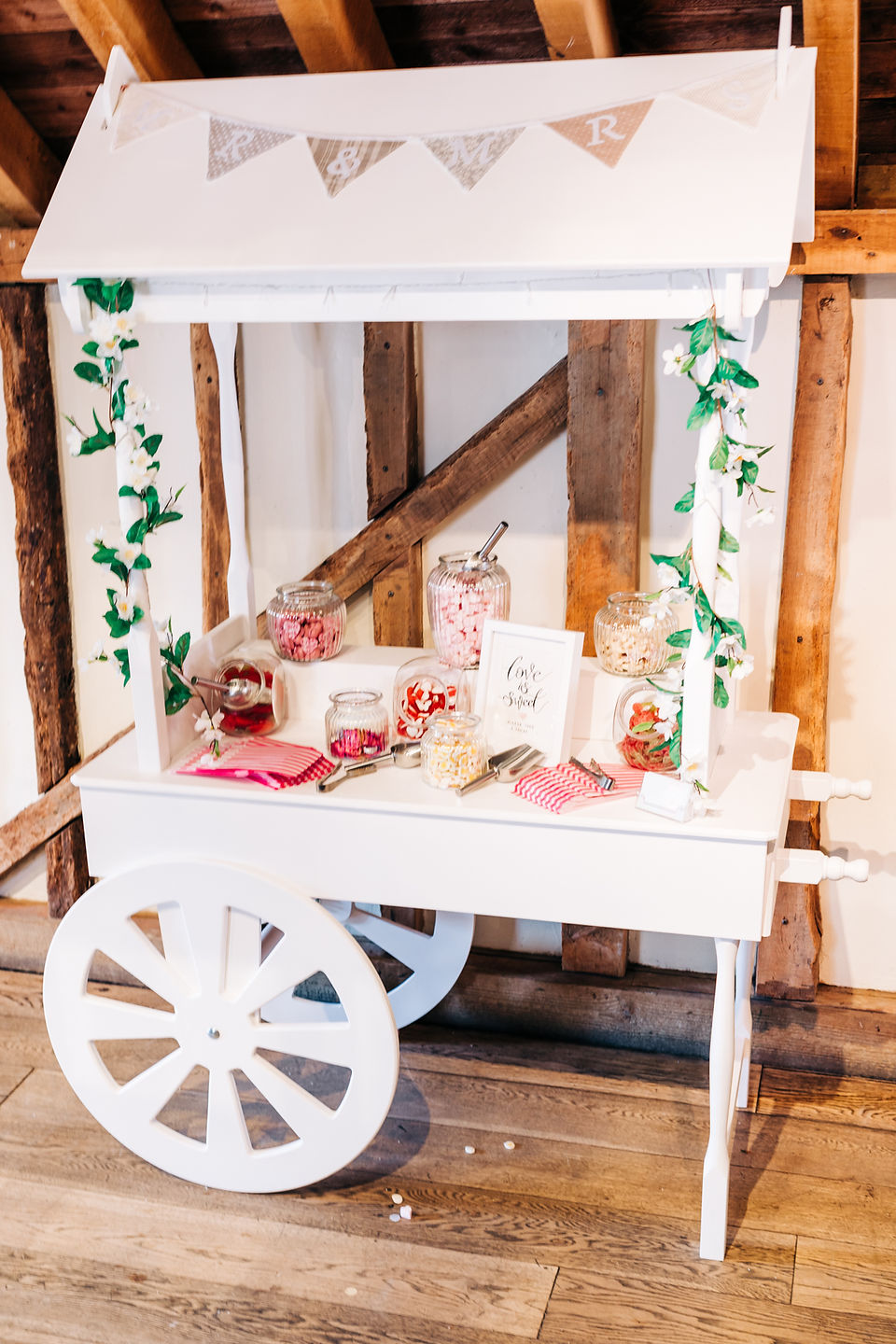 A white wooden sweet cart full of jars of pink and white sweets