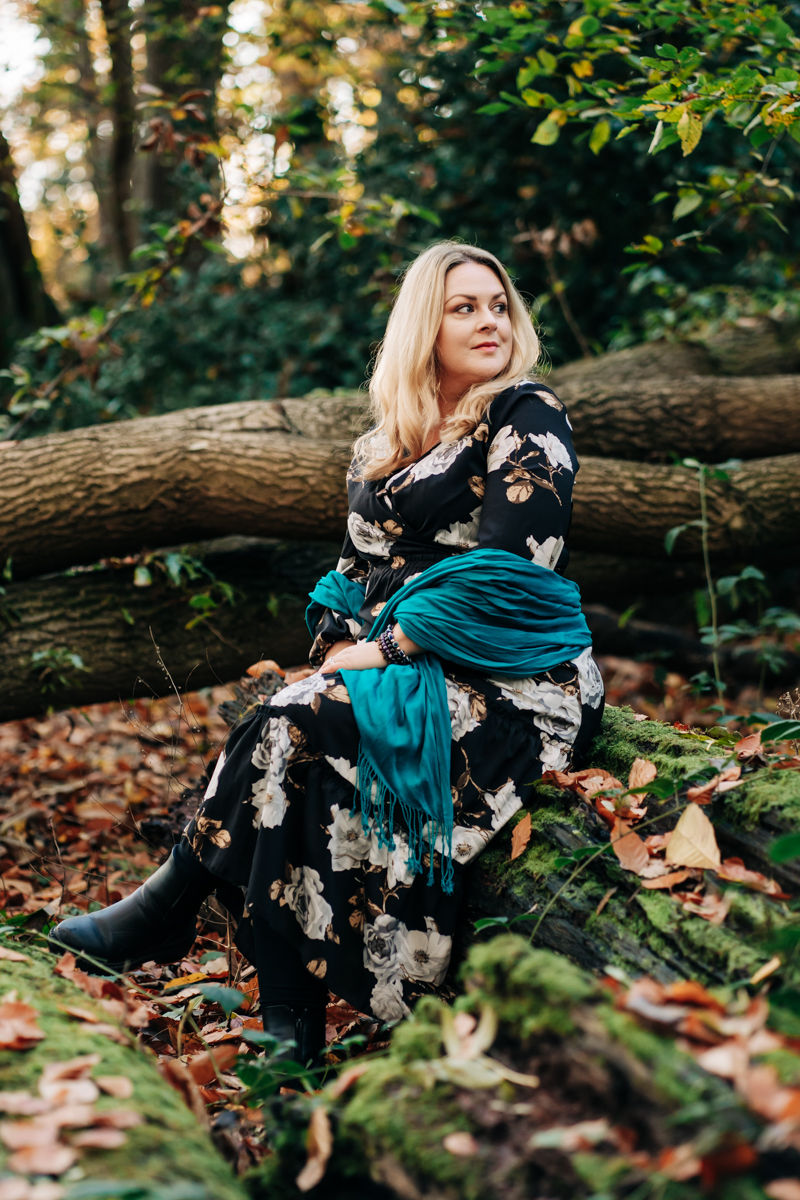 Sophia sitting on a moss-covered log with a fallen tree and greenery behind her