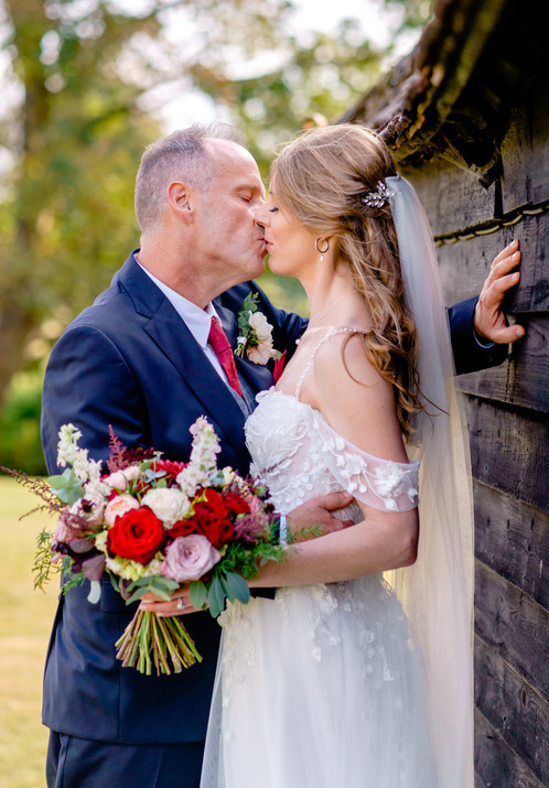 Bride leaning against a wooden barn wall being passionately kissed by groom