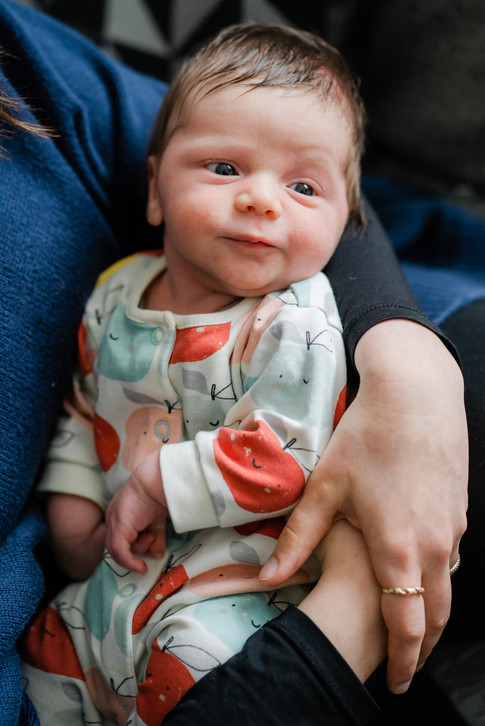 A newborn baby in a bright babygrow in his mother's arms, with a quizzical look on his face