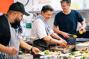 3 men in industrial kitchen sharing a joke as they plate up a main course dish