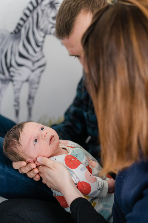 A mother and father cradling a newborn baby on their laps making eye contact with him