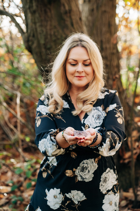 Sophia standing in a woodland in front of a large tree trunk, holding an amethyst.