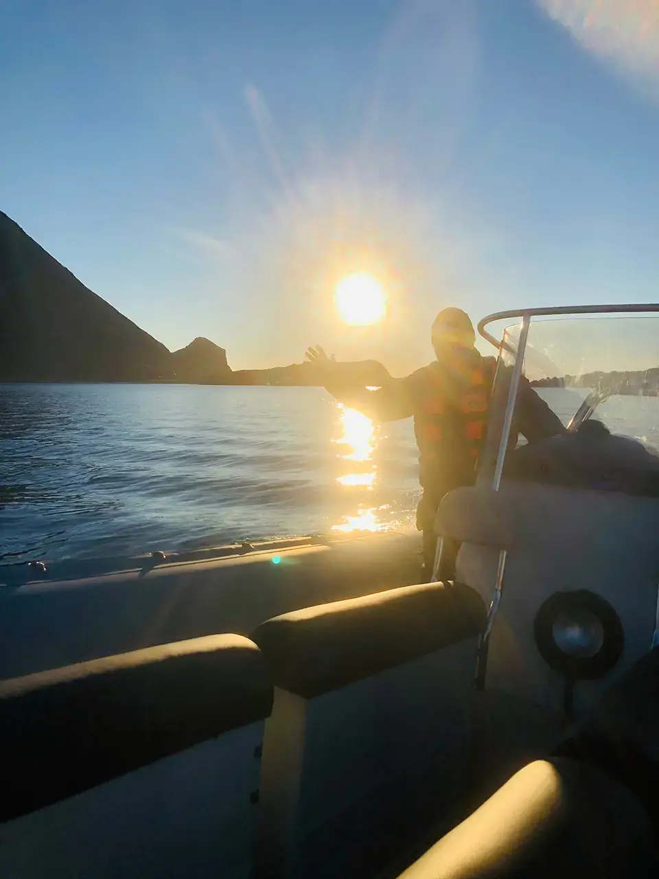 Person styrer motorbåt på vannet under en glødende solnedgang.
