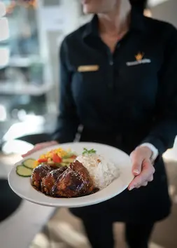 Servitør i svart uniform holder tallerken med grillet kylling, ris og grønnsaker.