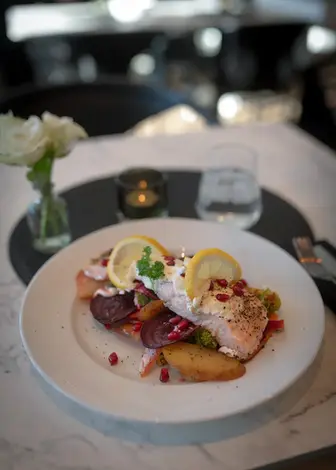 Laks på tallerken med sitron, poteter, grønnsaker på et elegant bord.