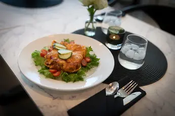 Elegant servert middagsrett med salat og vann på et marmorbord.