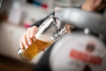 Hånd fyller et glass lyst øl fra en tappekran i baren.