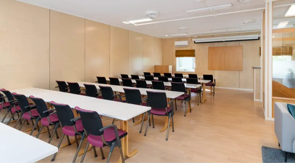 Moderne tomt møterom med prosjektorskjerm, bord og stoler.