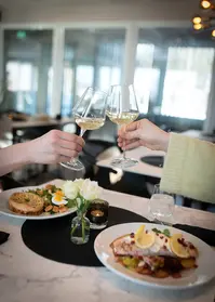 To hender skåler med hvitvin over fiskerett og salat på bord.