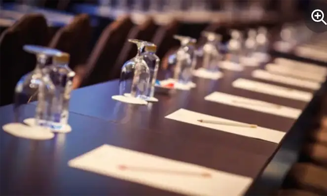 Langt møtebord med glass, notatblokker og penner klart for deltakere.