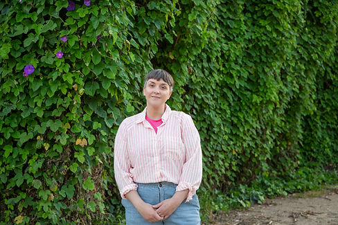 JD the Doula stands smiling gently in front of a wall of greenery