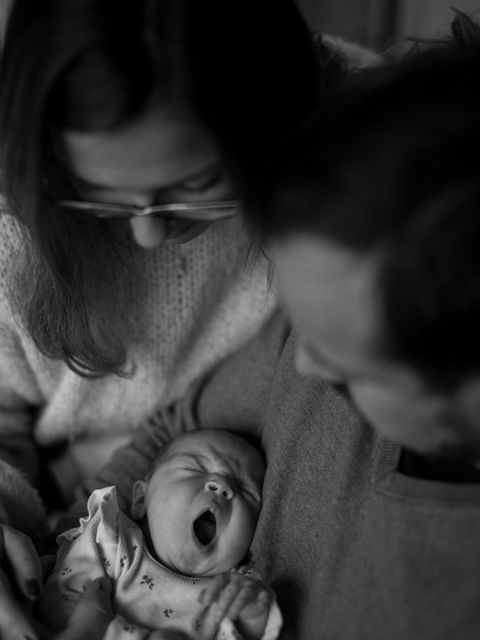 Schwarz-weiß Foto einer kleinen Familie. Aufnahme von oben, Fokus auf einem gähnenden Neugeborenen. Newborn Fotoshooting bei Scharbeutz