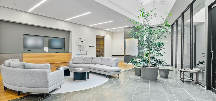 Bright, freshly cleaned office lobby with gray sofas, a large potted tree, and polished stone-tile floors under a skylight