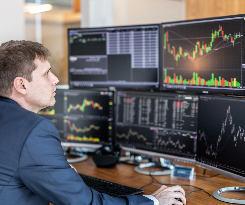 stock broker at his desk of 5 screens monitoring different charts.