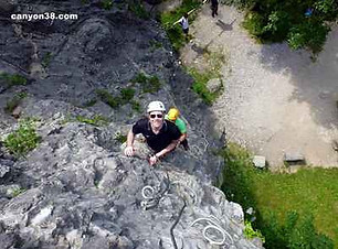 Adulte qui sourit face à la caméra en escaladant les barreaux de la via ferrata de la Bastille à Grenoble.