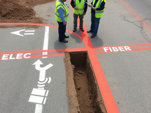 Construction crew reviewing underground utility markings with red electrical and orange fiber lines before trenching, showing proper utility marking and mapping to prevent construction delays.